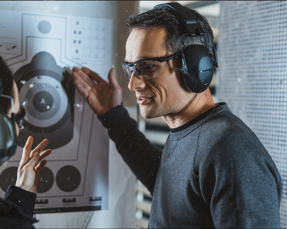 A male middle age man explaining a female about the shots shown on a shooting paper target inside a shooting range.