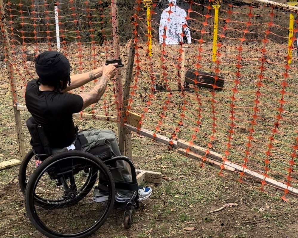 Man on a wheelchair at an outdoor gun range shooting his handgun at practice dummies. 