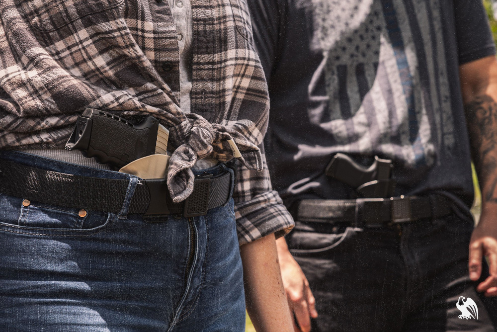 Man and woman outdoors in casual clothing and jeans, both wearing Vedder Belts and carrying LightTuck Kydex IWB holsters for concealed carry.