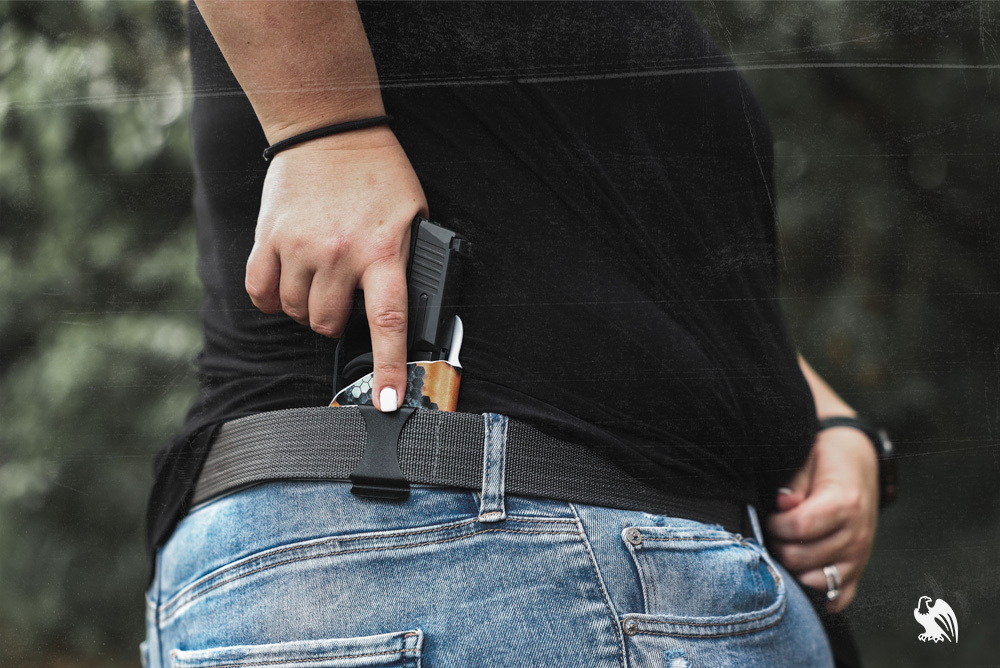 Curvy woman in jeans and a black shirt drawing her handgun from a Vedder LightTuck IWB holster, concealed at the 4 o’clock position, ideal for comfortable carry on curvier body types.