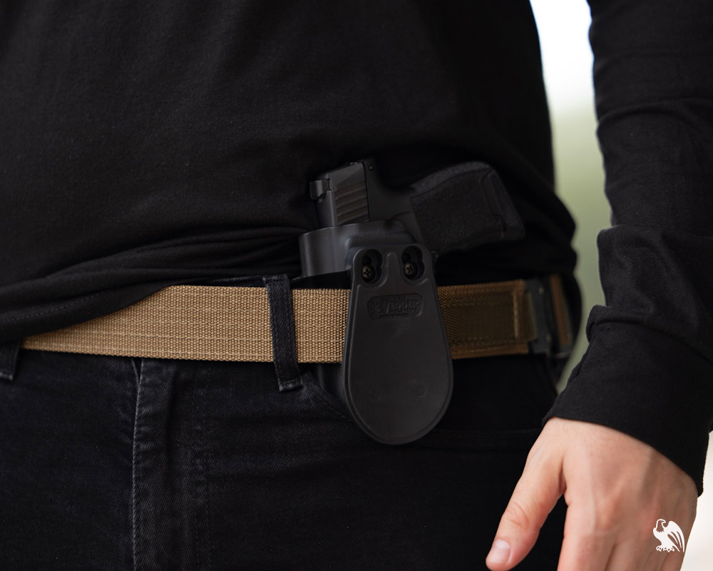 Vedder OWB paddle holster improperly worn inside the waistband on a tan tactical belt, demonstrating why OWB holsters aren't designed for IWB carry.