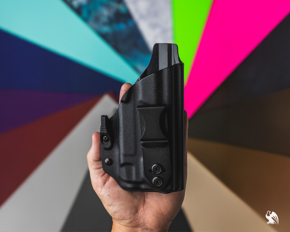 Man holding a Vedder LightTuck holster for the Kimber Micro 9 with colorful Kydex sheet options blurred in the background.