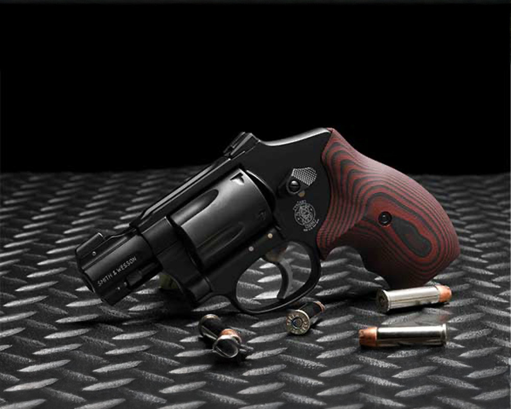 Smith & Wesson J-Frame revolver with red and black grip and .38 Special rounds on a steel surface.