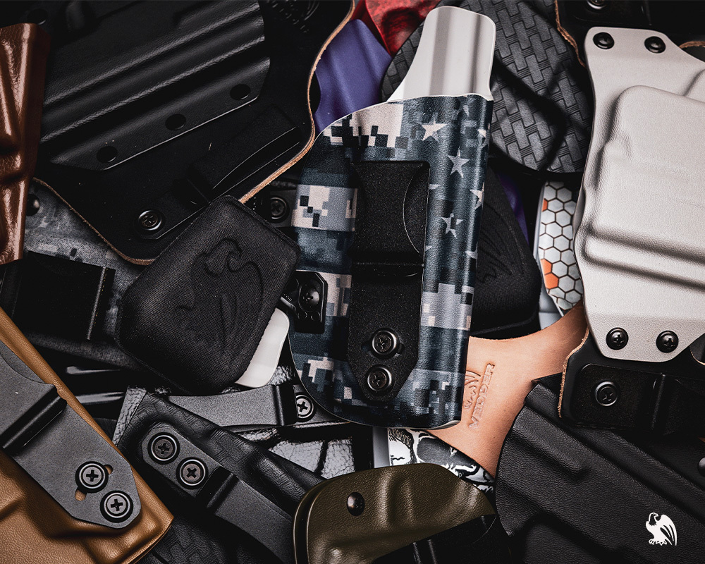 Several Kydex and Hybrid Holsters and a holster wedge layed out next and on top of each other. 