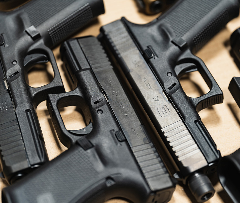 Close-up of multiple Glock pistols, including a Glock 45 9mm, displayed on a flat surface, highlighting textured grips, polymer frames, and slide serrations, ideal for firearm enthusiasts, gun safety training, or concealed carry discussions.