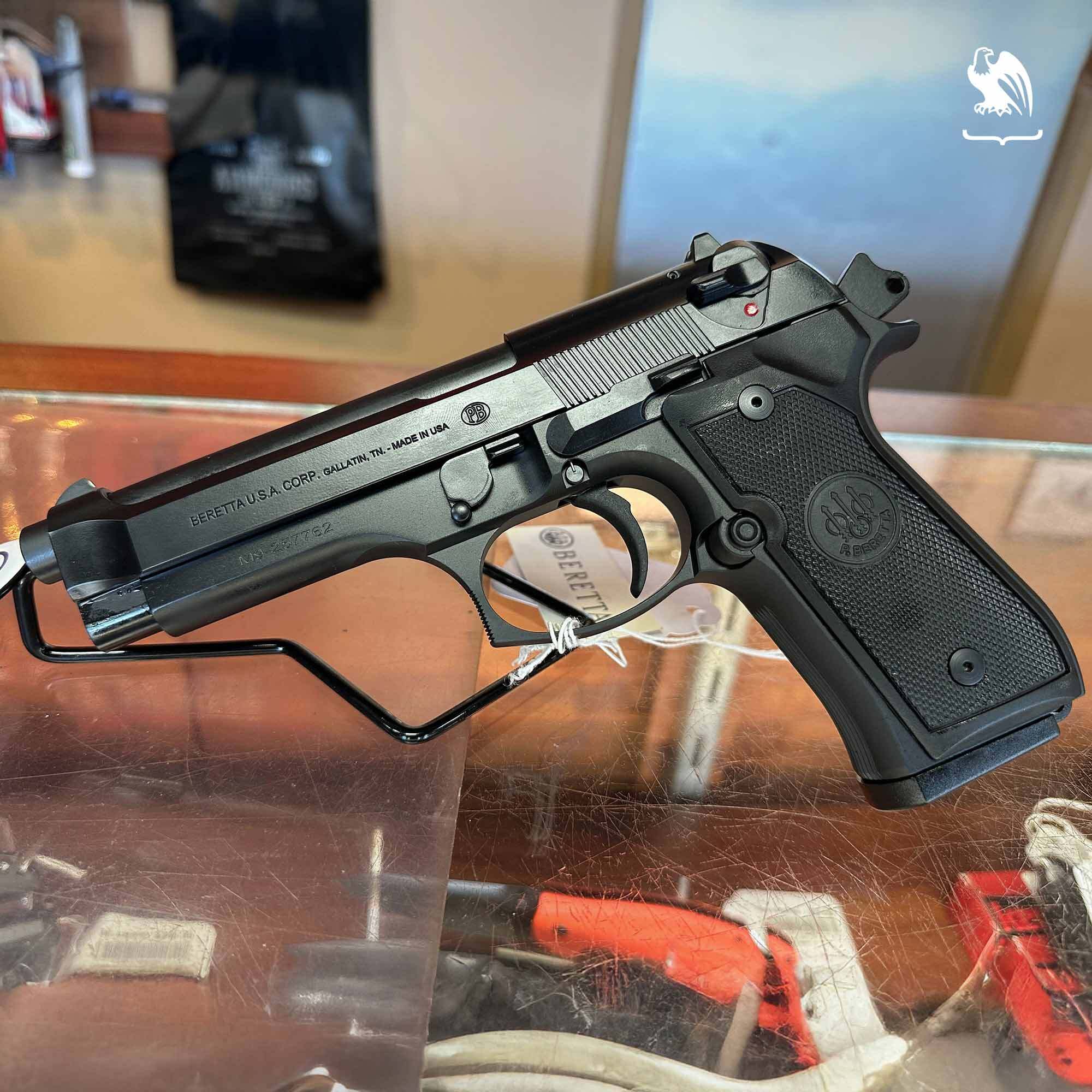 Beretta M9 semi-automatic handgun displayed on a retail counter, featuring a black finish, textured grip, and slide-mounted safety.