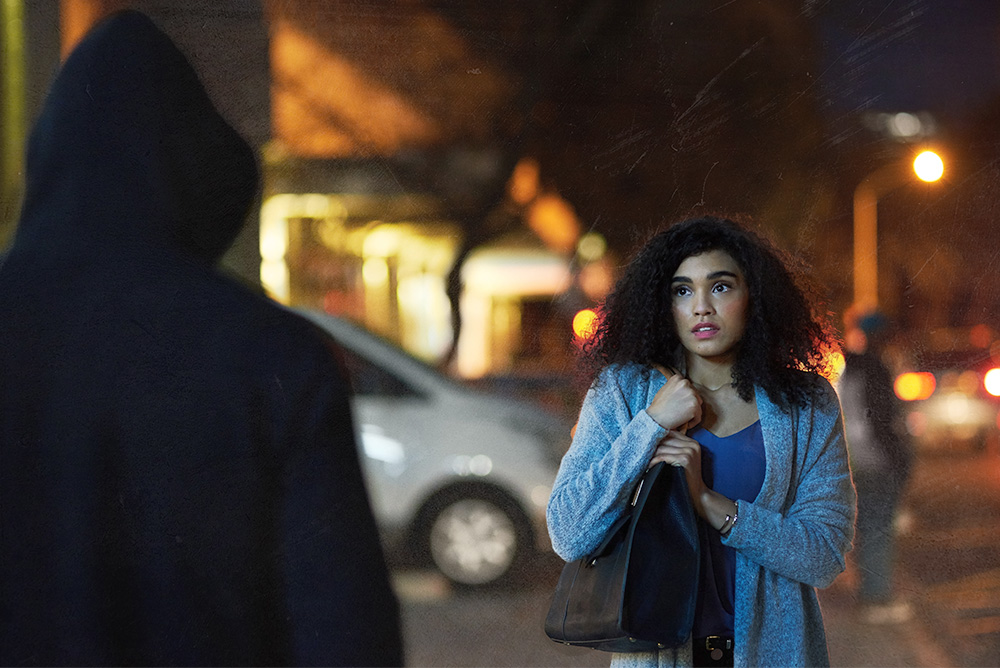 Man wearing a hoodie approaching a woman at night - Vedder Holster's Stock Photorgraphy