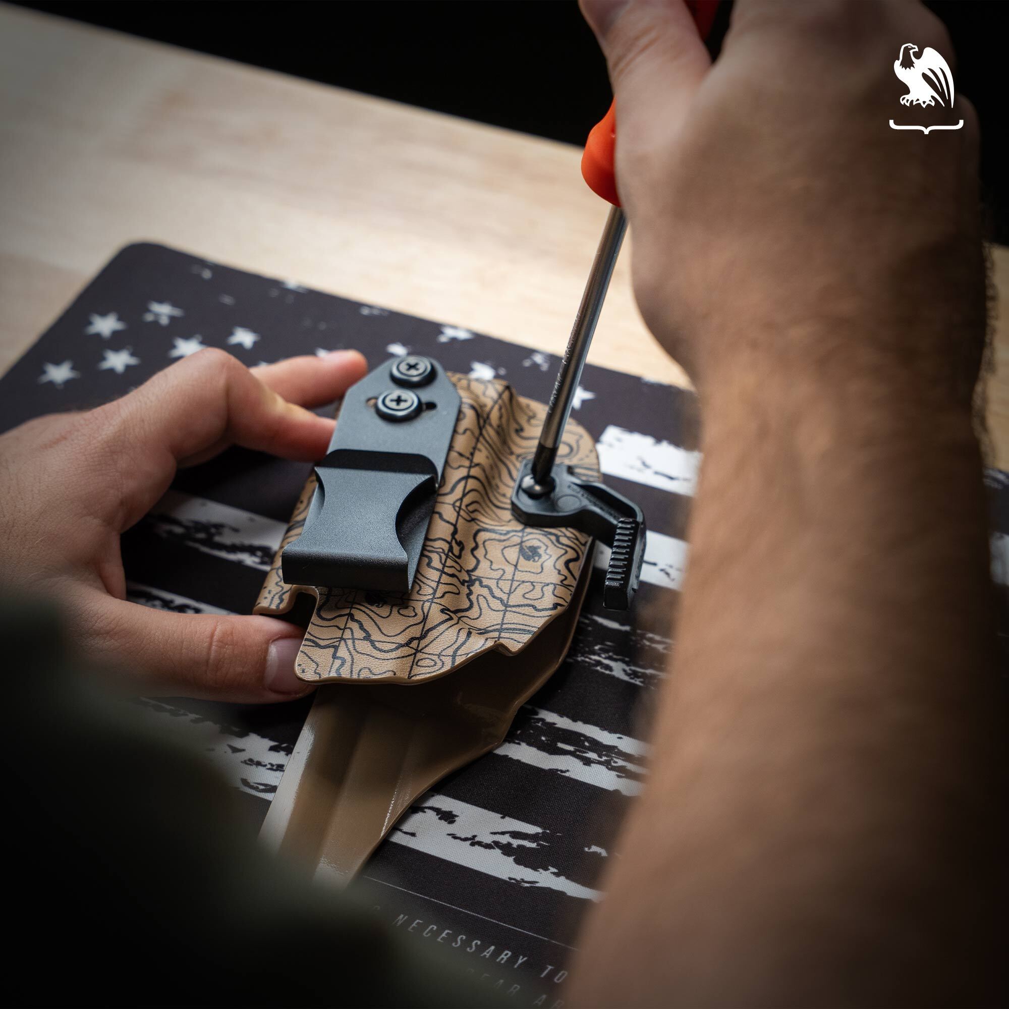 Tighten Retention A close-up of a man tightening the retention screw of a Vedder Holsters LightTuck on a Gun Cleaning Mat