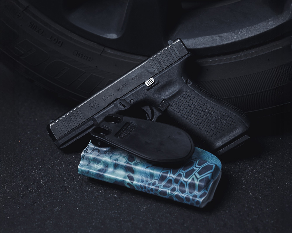 Glock 17 Gen 5 with blue Kryptek Kydex holster and paddle attachment near a tire, ready for everyday carry.