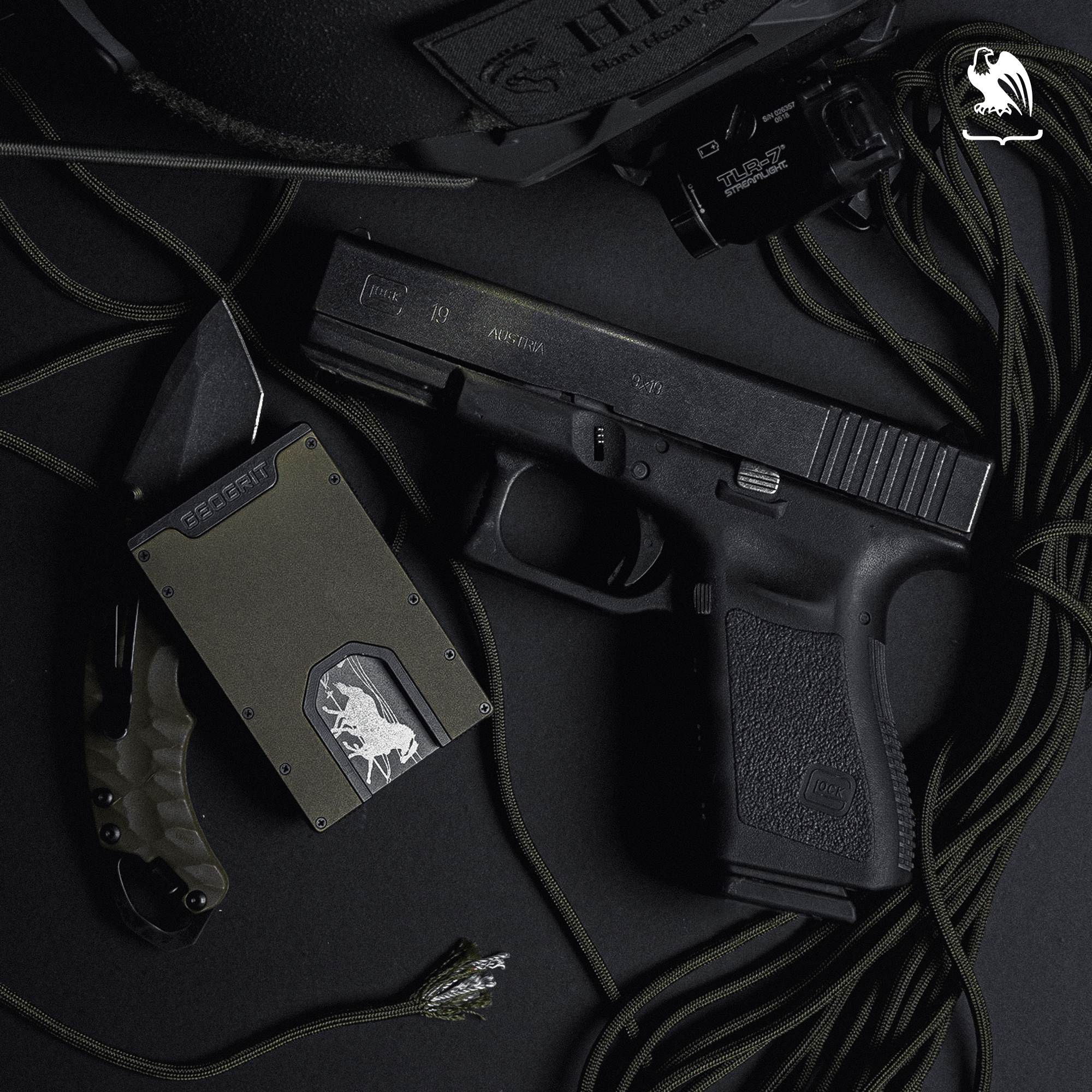 Glock 19 laying on black table next to a slim wallet and other tactical items