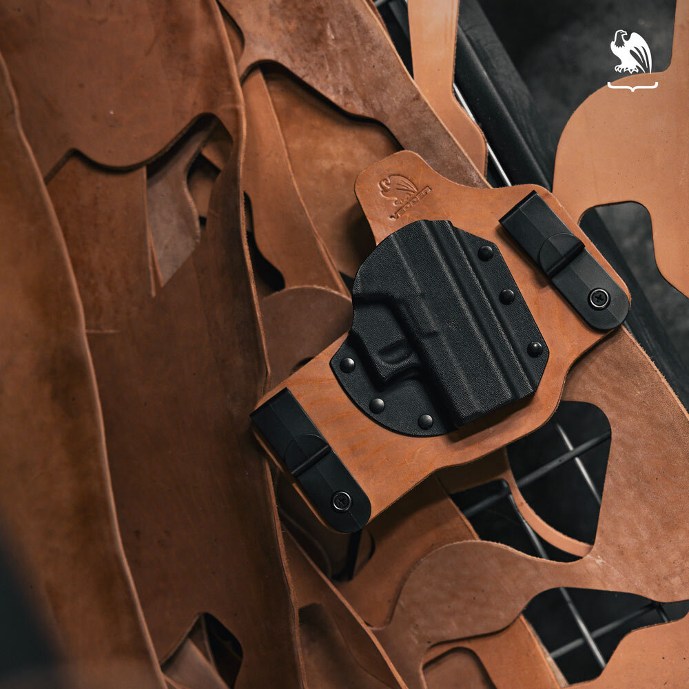 Hybrid leather and Kydex concealed carry holster displayed on Horween leather sheets, handcrafted by Vedder Holsters.