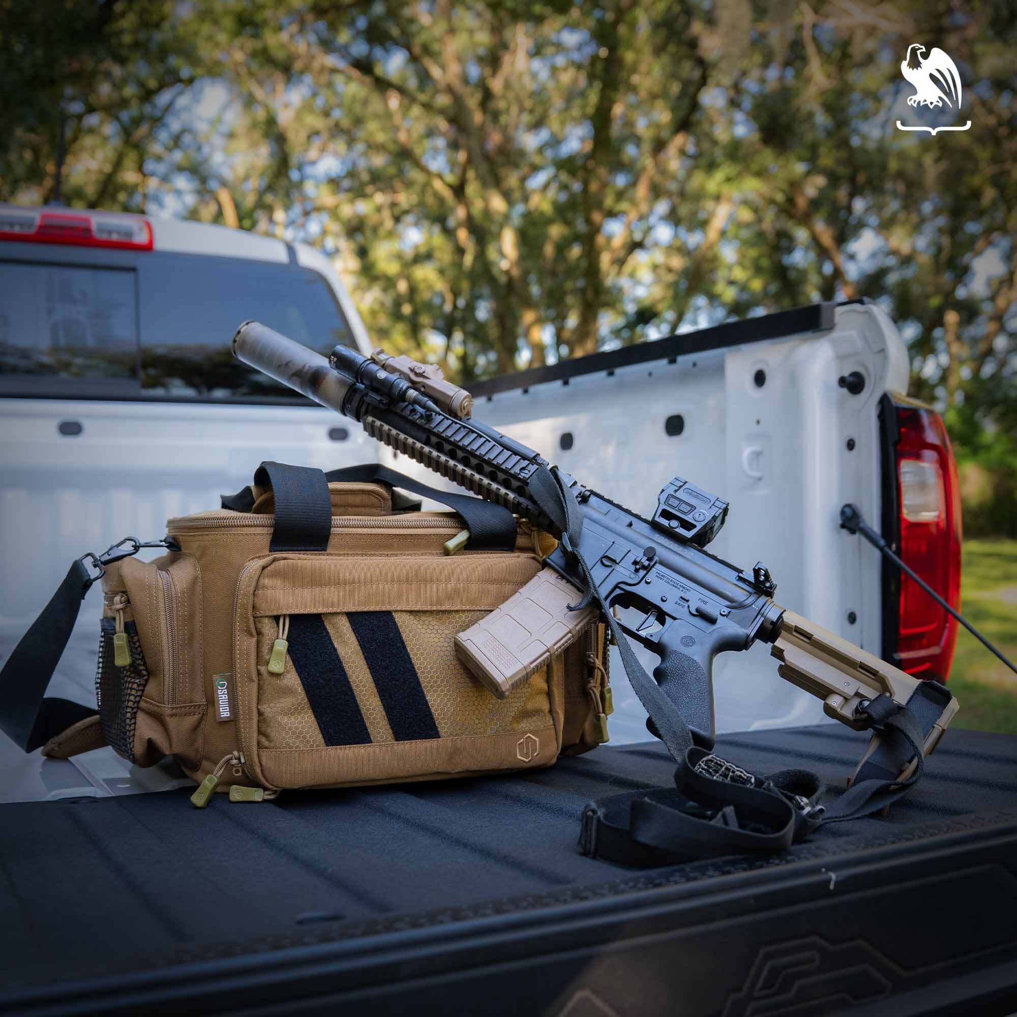 Rifle with Suppressor A rifle with a suppressor sits on the tailgate of a white truck with a tan range bag.