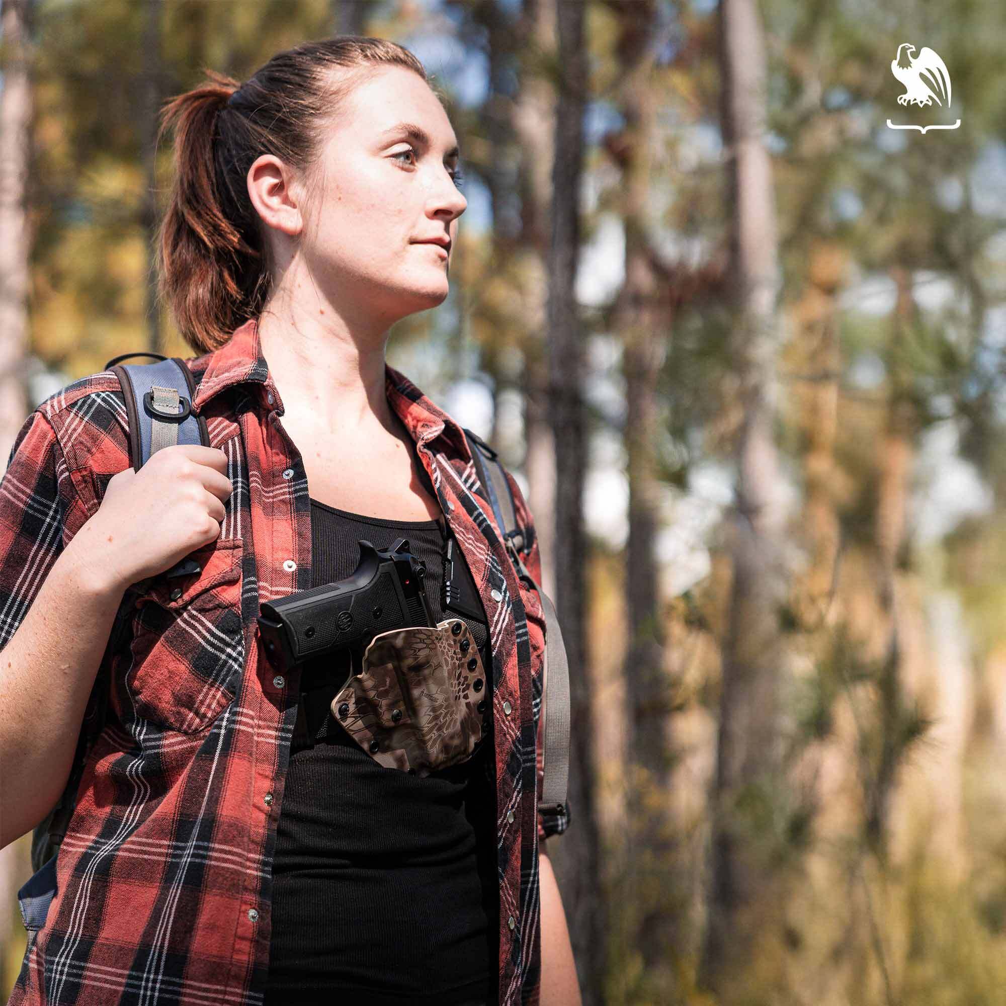 Red Flannel Chest Holster A woman in a red flannel shirt hikes through the woods carrying a pistol in a Vedder Holsters EverTrek Chest Holster