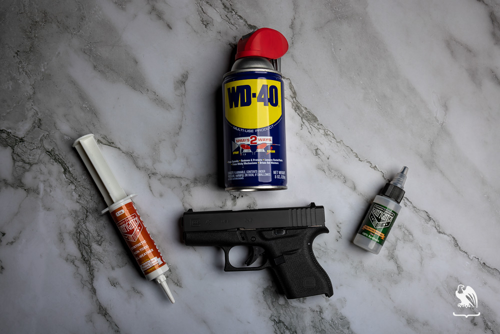 Items like WD-40 and gun oil used to clean a handgun all laying on top of a marble table