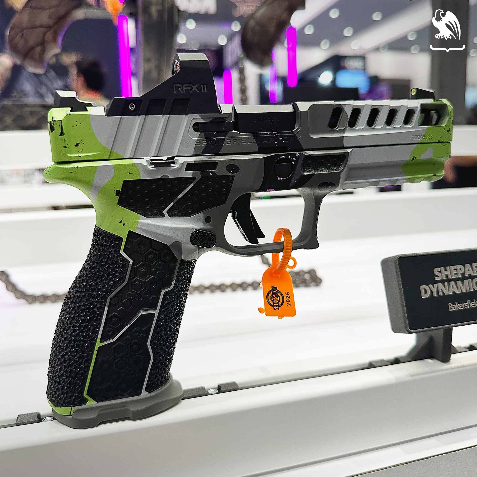 Custom competition handgun with gray and green camo finish, ported slide, reflex optic, and textured grip displayed at the SHOT Show trade event in Las Vegas.