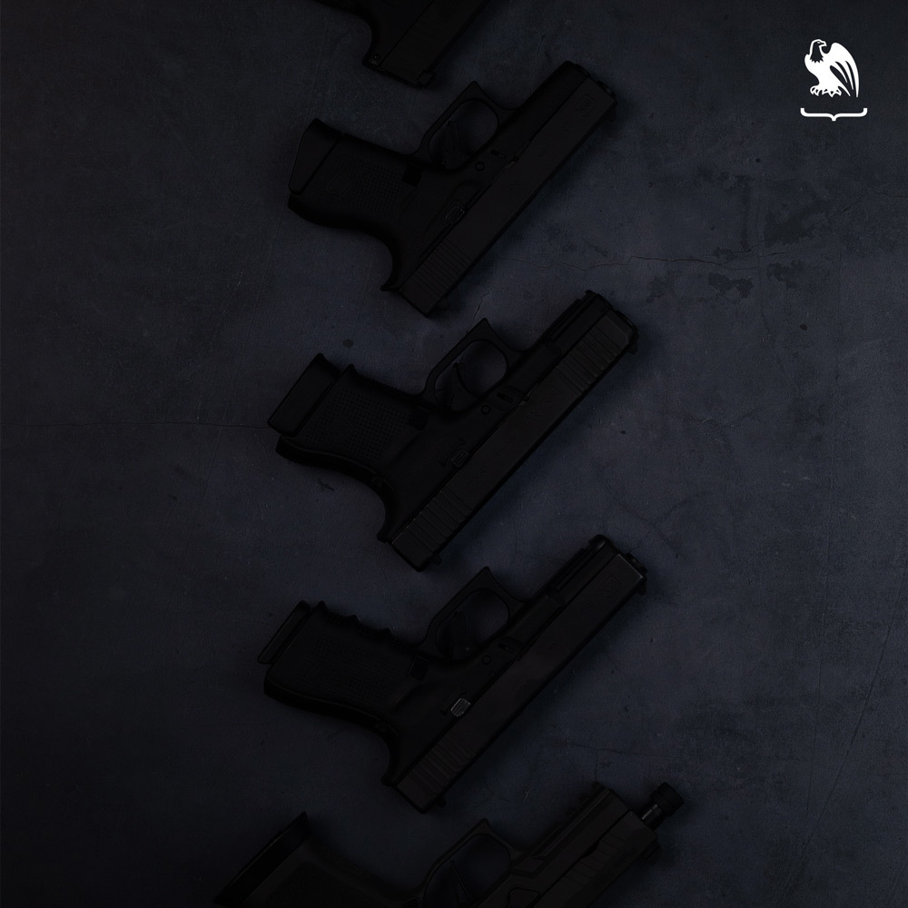 Flat lay of multiple Glock pistols arranged diagonally on a dark background, showcasing different handgun models in a clean, tactical layout.