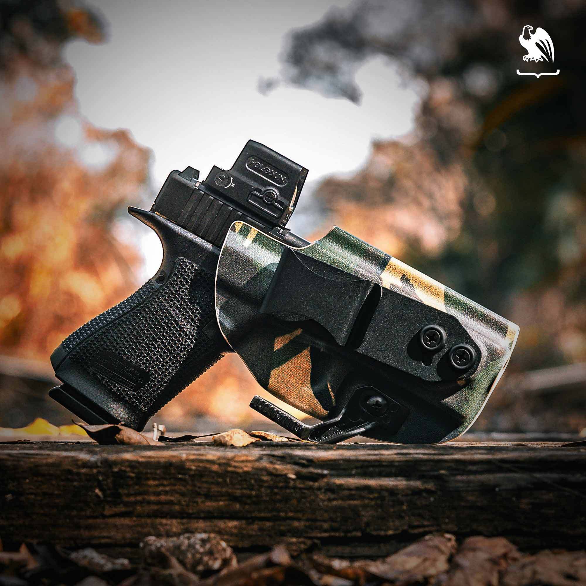A black pistol with a red dot sight in a camo Vedder Holsters LightTuck sitting on a railroad tie outside